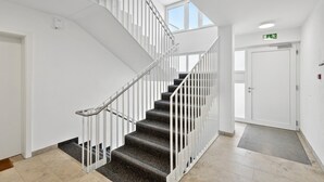 Een modern interieur met een trap, witte muren en een deur met een nooduitgangsbord.