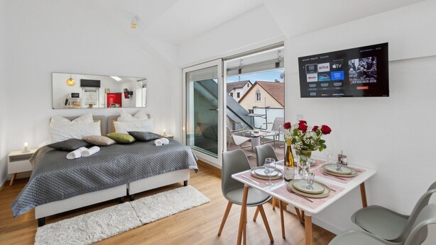 Een moderne slaapkamer met een bed, nachtkastje en een aan de muur bevestigde televisie.