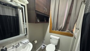 Et badeværelse med en hvid vask, et toilet og et spejl. Der er en håndklædeholder over vasken og en badeforhæng.
