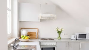 A modern kitchen with a sink, stove, oven, microwave, and a bowl of fruit on the counter. - Ferienwohnung Villy Seepark – mit Balkon & Parkplatz (Heringsdorf)