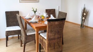 A dining area with a wooden table, wicker chairs, a hanging light fixture, and a framed picture on the wall. - Ferienwohnung Villy Seepark – mit Balkon & Parkplatz (Heringsdorf)