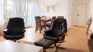 A spacious living area with a dining table, two leather chairs, and a large window with curtains. - Ferienwohnung Villy Seepark – mit Balkon & Parkplatz (Heringsdorf)