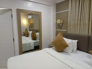 A hotel room with a bed, a mirror, a window with curtains, and a wall-mounted lamp. - HARIS HOTEL (Abuja)