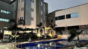 A multi-story building with a swimming pool, palm trees, and a brick wall. - HARIS HOTEL (Abuja)