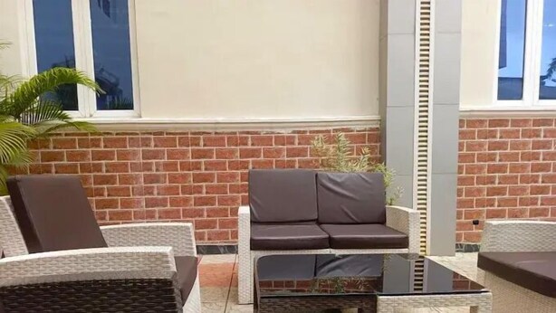 An outdoor seating area with wicker furniture and a brick wall backdrop. - HARIS HOTEL (Abuja)