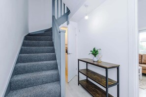 En trappa med ett grått, heltäckande mattgolv, ett metallräcke och ett litet bord med en växt bredvid.