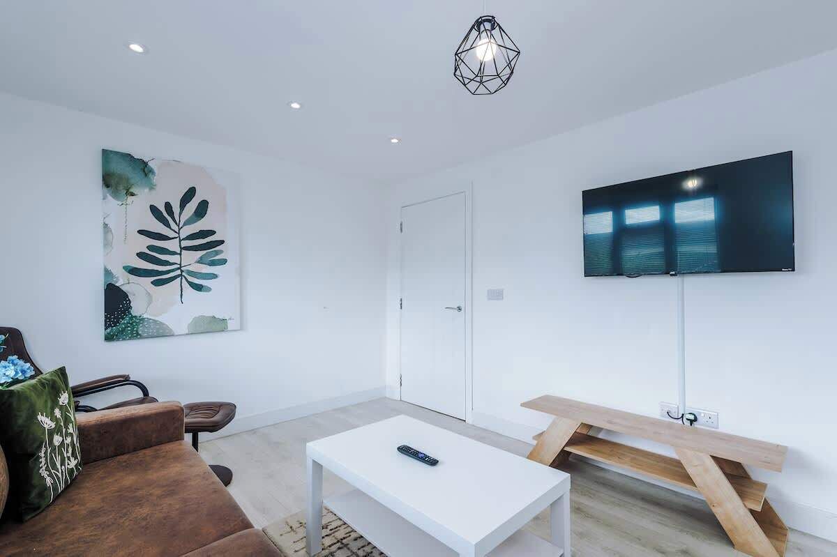 A modern living room with a white sofa, a coffee table, a TV mounted on the wall, and a painting.