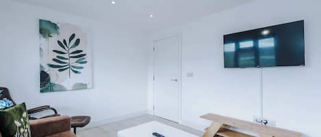 Una sala de estar moderna con un sofá blanco, una mesa de centro, un televisor montado en la pared y un cuadro.