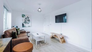 A modern living room with a sofa, coffee table, and a TV mounted on the wall. - Elegant Spacious 3BR | Shrewsbury w/ Free Parking (Shropshire)