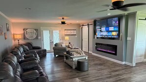 Una sala de estar moderna con un sofá seccional, una chimenea, un televisor de pantalla plana y un ventilador de techo.