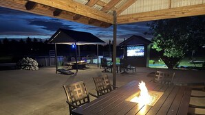Un espacio al aire libre con patio que incluye una mesa con fogón, sillas y una zona de estar techada.
