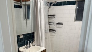 A bathroom with a white sink, wooden vanity, white toilet, and a bathtub. - North Pacific Beach - a cozy, 1-bedroom designed for rest, & recharge. (San Diego)