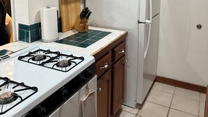 A kitchen with wooden cabinets, a white refrigerator, a gas stove, and a wooden cutting board. - North Pacific Beach - a cozy, 1-bedroom designed for rest, & recharge. (San Diego)