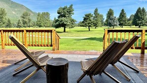 Een terras met twee houten stoelen en een houten tafel, met uitzicht op een grasveld en bomen.