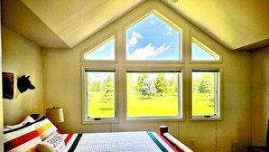 Een slaapkamer met een groot bed, meerdere ramen en uitzicht op een groen veld.