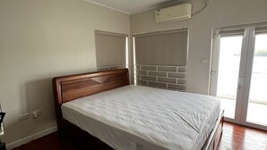Un dormitorio con cama de madera, ventilador de techo, aire acondicionado, una ventana y una puerta.
