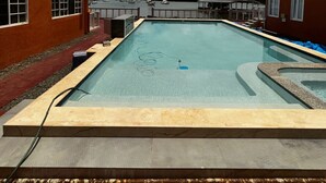 Una piscina rectangular con superficie de agua azul cristalina, rodeada de edificios de ladrillo rojo con múltiples ventanas.