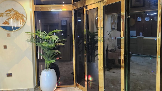 A hotel entrance with a large potted plant, a wall-mounted clock, and a glass door leading inside.