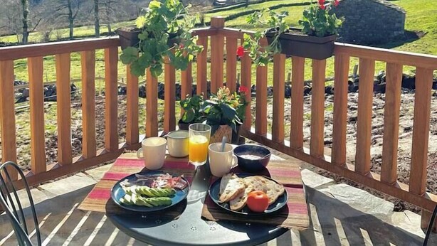 Ett bord uppdukat utomhus med en vacker utsikt över bergen, ett trästaket och krukväxter.