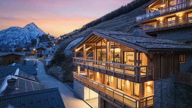 Una cabaña de madera con balcón que da a una montaña nevada.