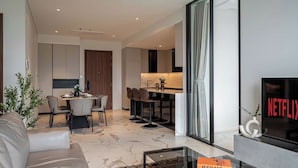 A modern living room with a sofa, a glass coffee table, and a dining area with chairs and a table. - Luxury Apartment Hotel - The Metropole (Ho Chi Minh City)