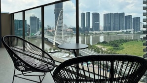 A balcony with two black wire-framed chairs and a small round table, overlooking a river with a bridge and high-rise buildings in the background. - Luxury Apartment Hotel - The Metropole (Ho Chi Minh City)