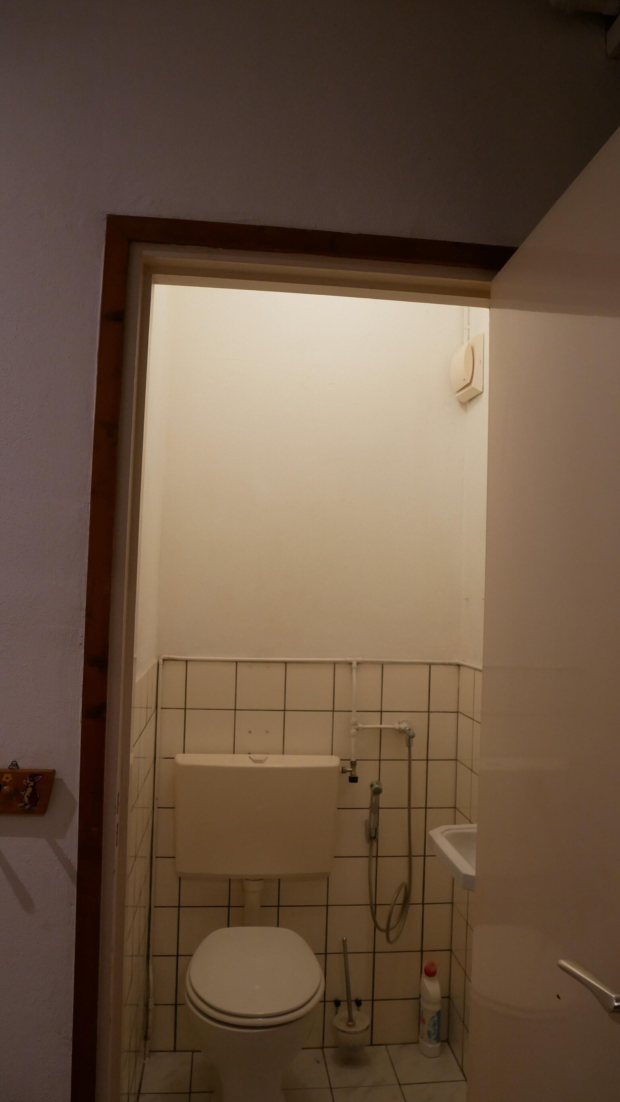 A small, dimly lit bathroom with a toilet, a shower, and a sink.