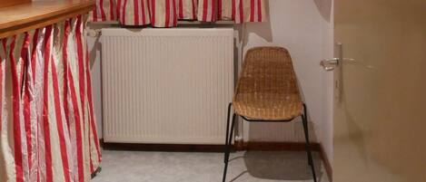 Una stanza con un termosifone, una sedia in vimini, una tenda a righe e un tavolo di legno.