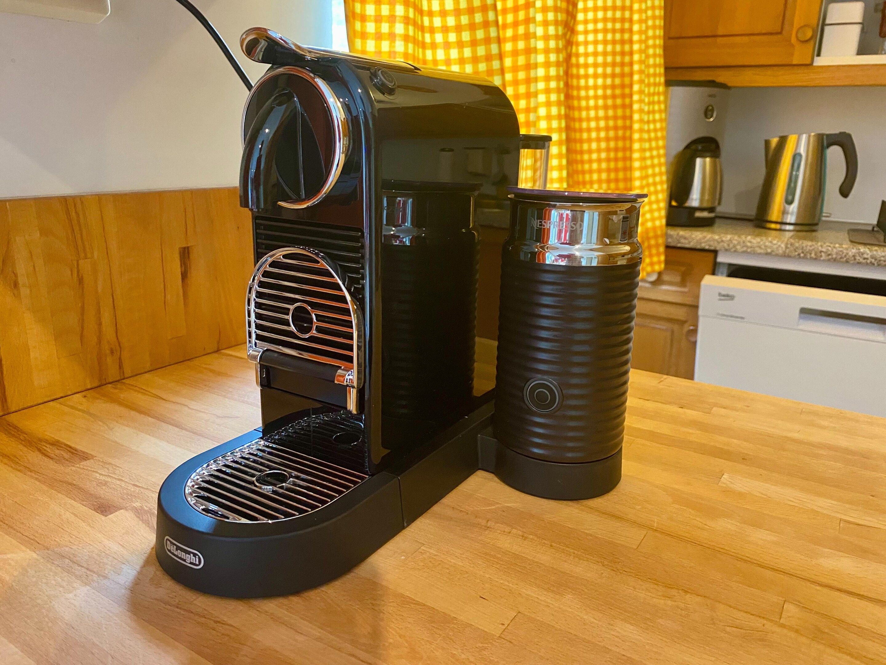 Une machine à café posée sur un plan de travail en bois, avec une bouilloire et un thermos à proximité.