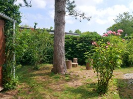 Un jardín con un árbol grande, plantas florecientes y una estructura de madera.