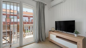 Ein Zimmer mit einer Schiebetür zum Balkon, einem Flachbildfernseher auf einem Holz-TV-Möbel und einer Topfpflanze auf dem Möbel.