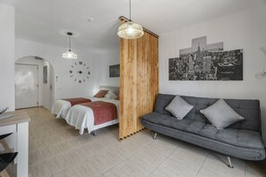 A modern room with a bed, a grey sofa, a wooden partition, a cityscape painting, and a wall clock.