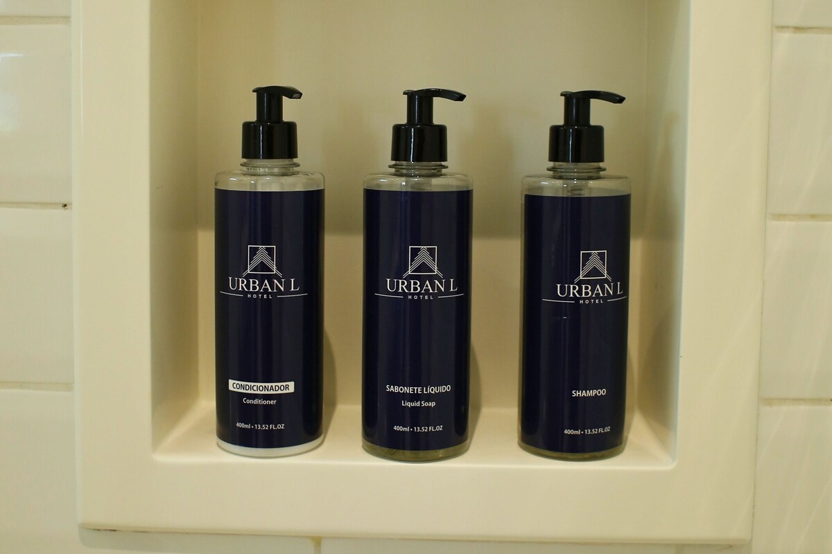 A bathroom shelf with three bottles of Urban Hotel products: conditioner, liquid soap, and shampoo.