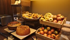 Un bufé de desayuno con diversos productos de panadería, frutas y una cesta de pan.