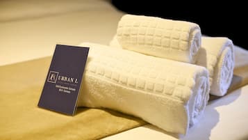 A neatly folded white towel with a tag labeled "URBAN L" on a bed.