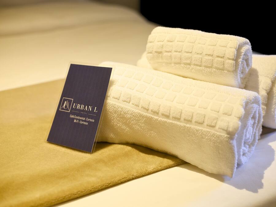 A neatly folded white towel with a tag labeled "URBAN L" on a bed.
