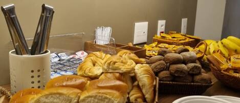 A buffet with various breads, pastries, and a stack of white plates.