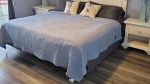Un dormitorio con una cama, dos mesitas de noche, un ventilador de techo y un cuadro en la pared.