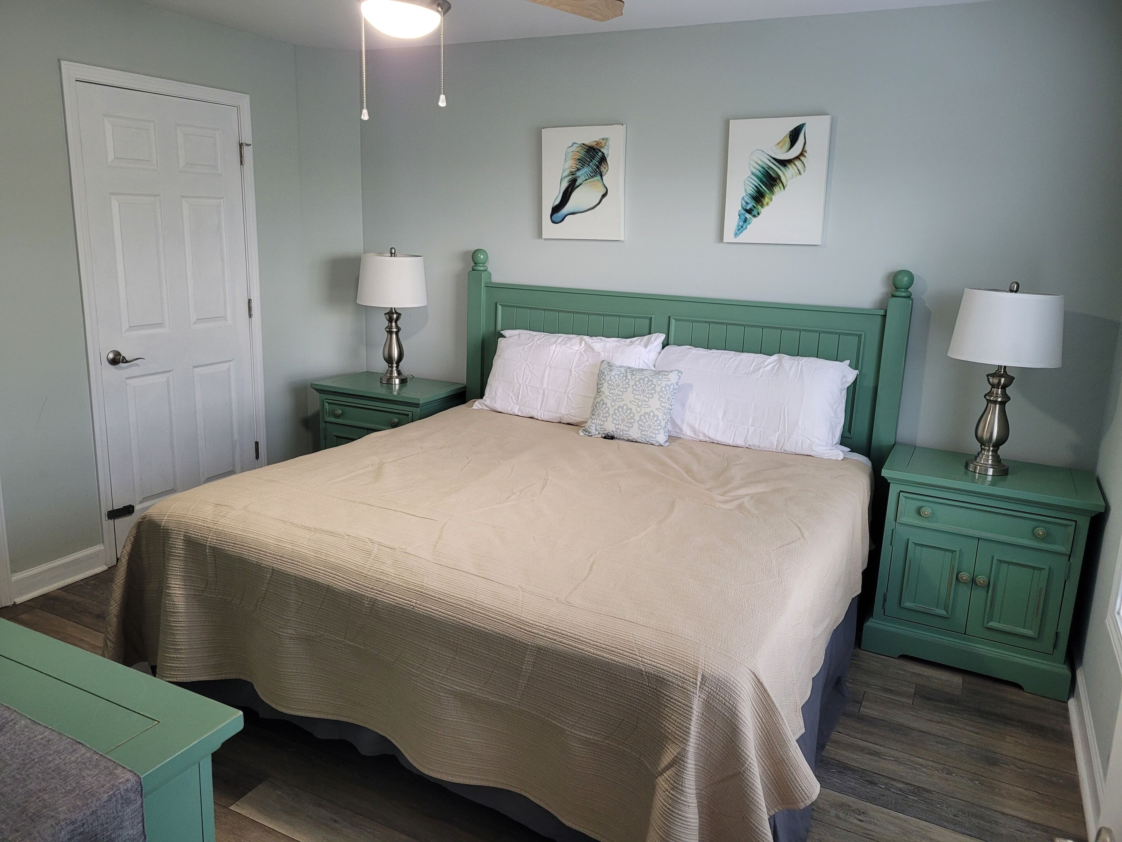 A bedroom with a large bed, two nightstands, a door, and two wall-mounted lamps.
