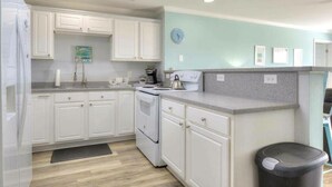 Una cocina compacta con gabinetes blancos, encimera de granito, estufa y un cubo de basura.