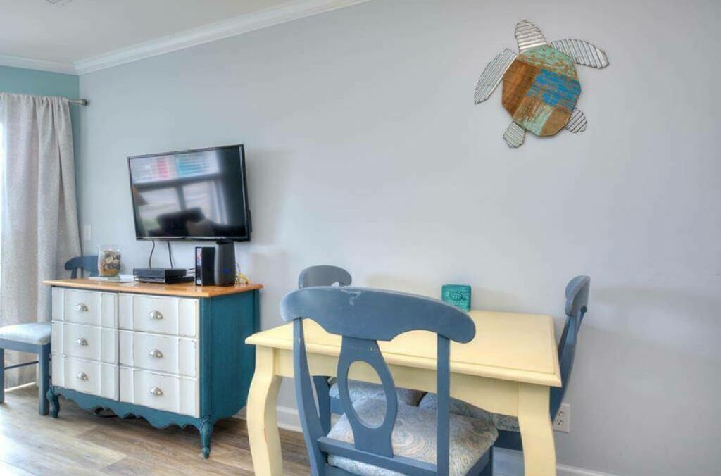 A dining area with a table and chairs, a television on a cabinet, and a wall decoration.