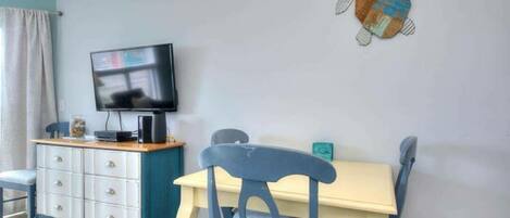 A dining area with a table and chairs, a television on a cabinet, and a wall decoration.