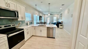 A modern kitchen with white cabinetry, a stainless steel dishwasher, and a black stove. - Docked at Dakota Sunset - Mid Island Pool Home (Fort Myers Beach)