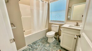 A bathroom with a bathtub, toilet, sink, and a window with blinds. - Docked at Dakota Sunset - Mid Island Pool Home (Fort Myers Beach)