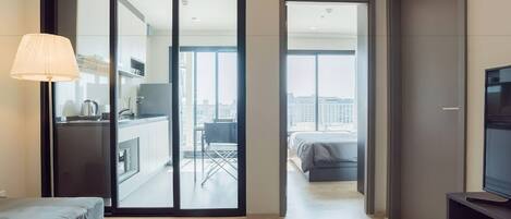 A modern hotel room with a sliding glass door leading to a balcony, a flat-screen TV, and a minimalist design.