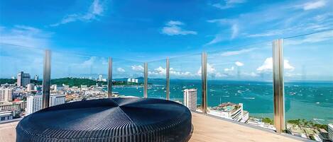 A high-rise room with a panoramic ocean view, a round black seating area, and large floor-to-ceiling windows.