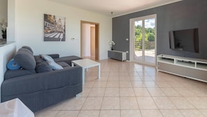 Ein modernes Wohnzimmer mit einem grauen Sofa, einem weißen Couchtisch, einem Flachbildfernseher und einer Glastür, die auf einen Balkon führt.