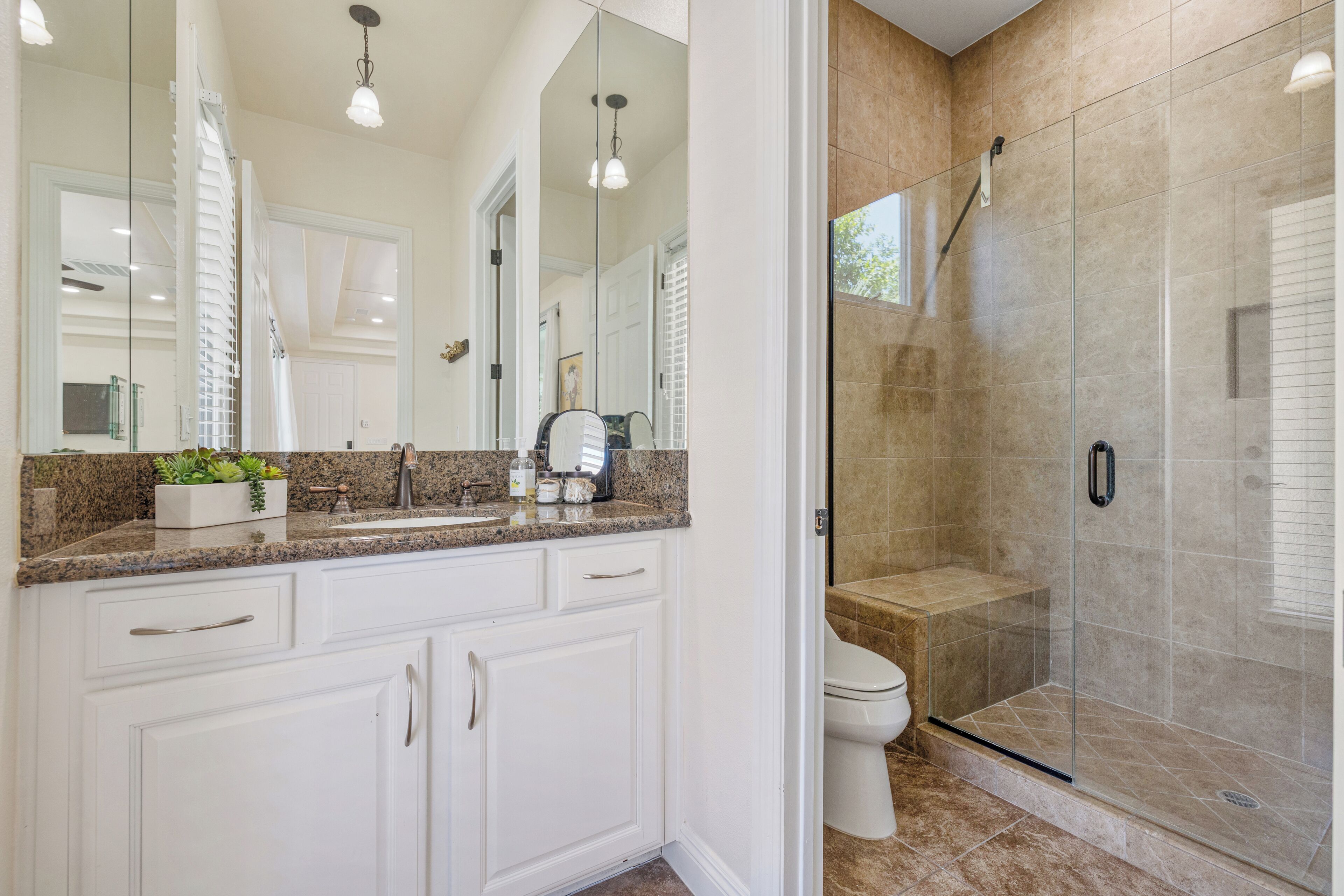 A bathroom with white cabinets, a granite countertop, a glass shower enclosure, and a toilet.