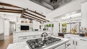 A modern kitchen with white cabinetry, a central island with a stove, and pendant lighting. - Velvet Palm - Elegant Oasis in Indian Wells (Indian Wells)
