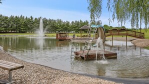 Een park met een vijver, een houten terras met een ladder, een kiosk en een brug.